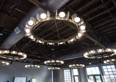 Large industrial style chandeliers hang from an open rafter ceiling with cool style, installed by Robinson Electric at Cotton House