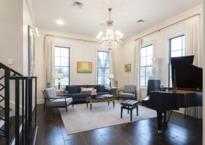 Chandelier and built in light fixtures within a home's living room with a large piano and windows