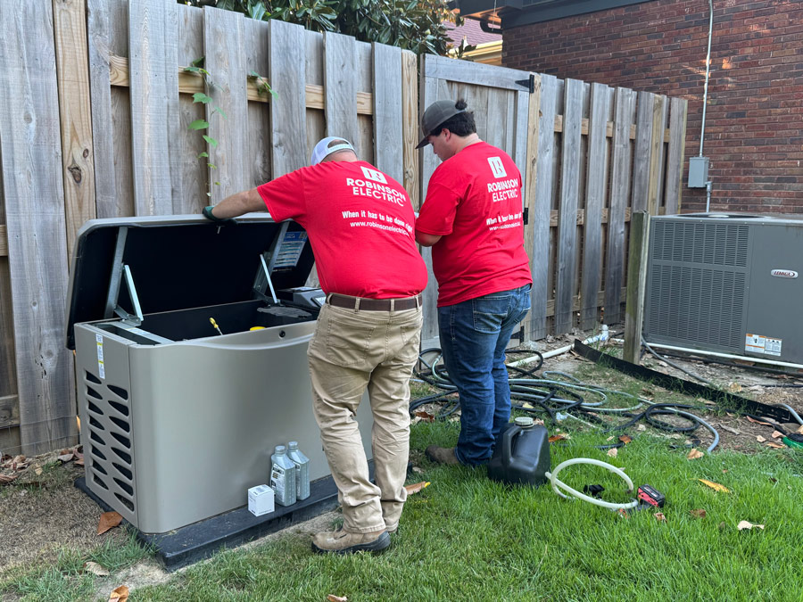 Two Robinson Electric workers in their red work shirts are installing a generator near a home.