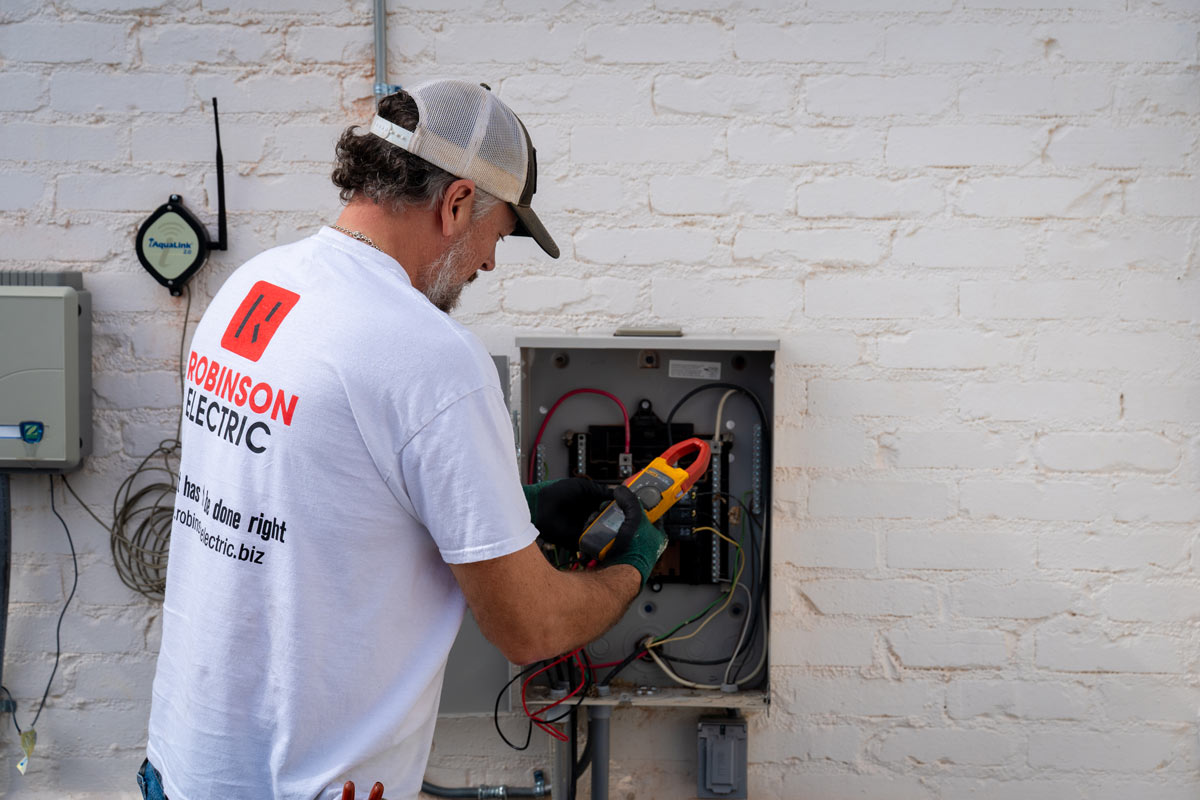 An electrician wearing a white Robinson Electric shirt works on an electric panel.